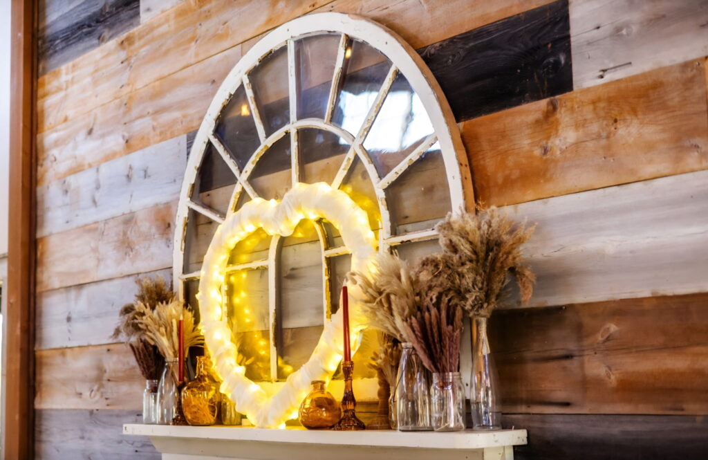 Rustic wedding decor with a lit wreath and pampas grass on a barnwood wall
